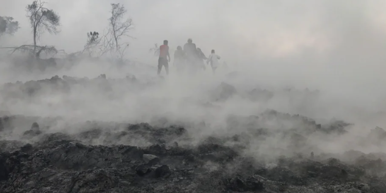 People are seen walking near smoldering ashes early morning in Goma in the East of the Democratic Republic of Congo on May 23 following the eruption of Mount Nyiragongo | AFP