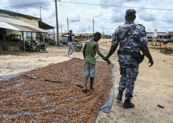 A police officer with a child who was drying cocoa in the sun | AFP