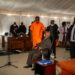Ex-president Guebuza, seated, talks to his son Ndambi Guebuza, wearing an orange prison uniform. The younger Guebuza is a defendant in the long-awaited trial, which is unfolding in a marquee in a high-security jail | AFP