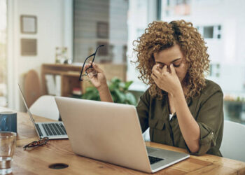 Shot of a young woman suffering from stress while using a computer at her work desk
