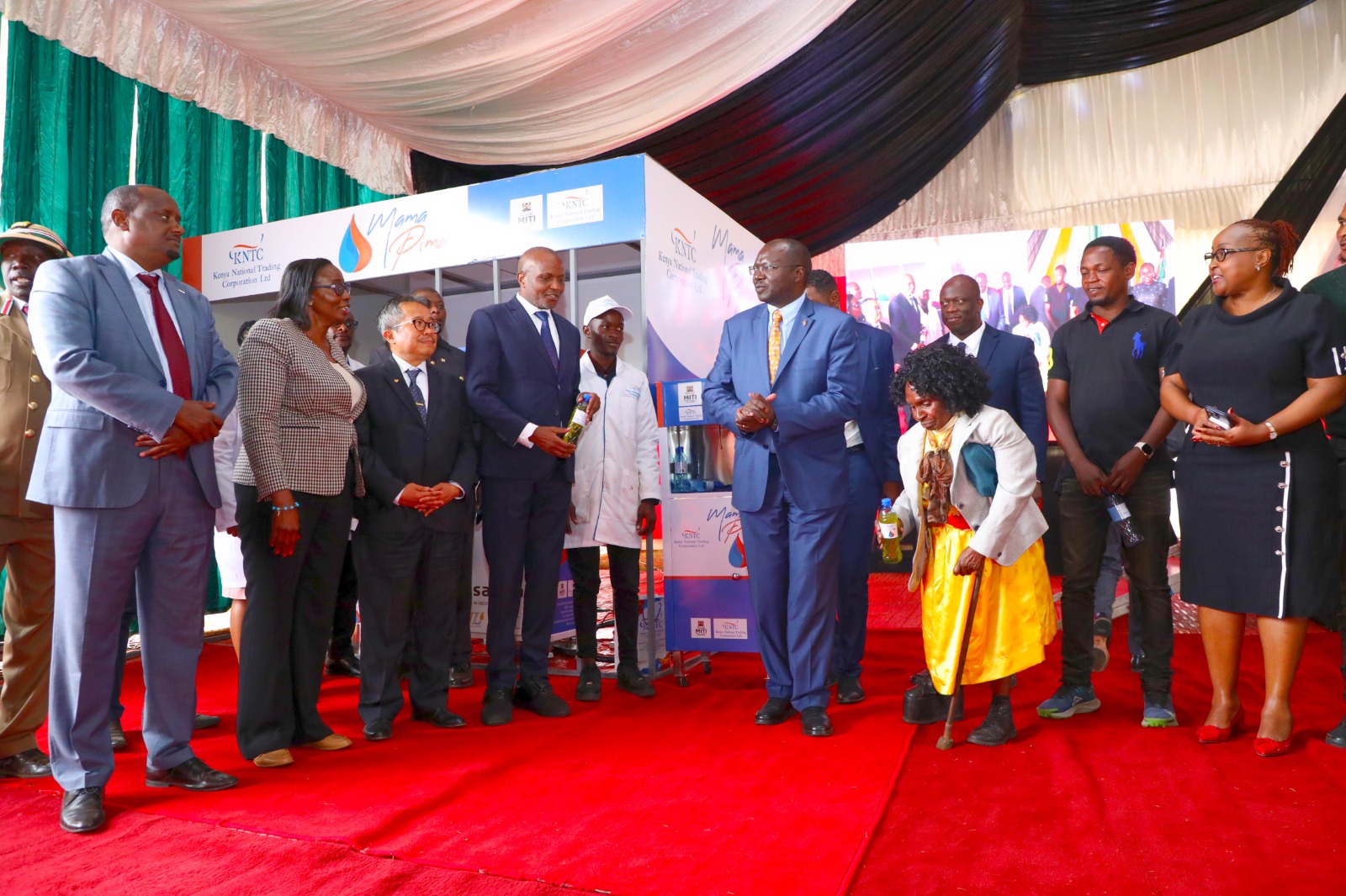 Trade Cabinet Secretary Moses Kuria (holding a bottle) joins other government officials and Kenyans during the launch of the Mama Pima dispensers. 