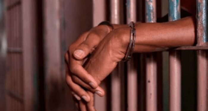 Gang leader arrested. A photo of person's hands resting on jail bars at a police station.